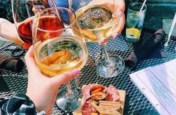 Hands holding two glasses of white wine and one glass of red cheers over a plate of meat and cheese
