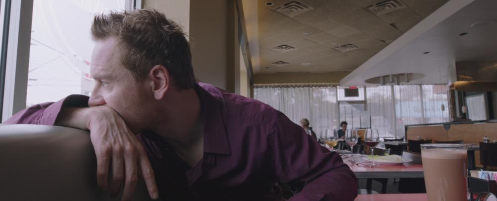 Song to Song screengrab, showing Cook sitting in a booth inside ASTI Trattoria while looking out the window behind him