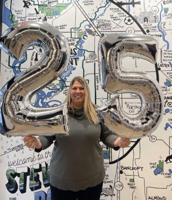 Executive Director Sara Brish holds up large silver 2 and 5 balloons to celebrate her 25th work anniversary milestone