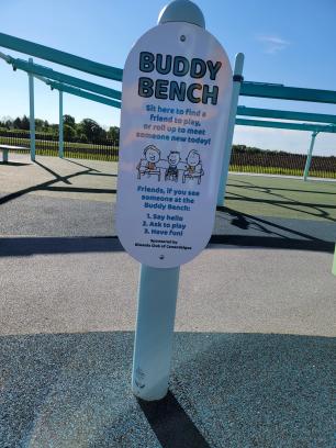 Buddy Bench Sign reads sit here to find a friend to play, or roll up to meet someone new today!