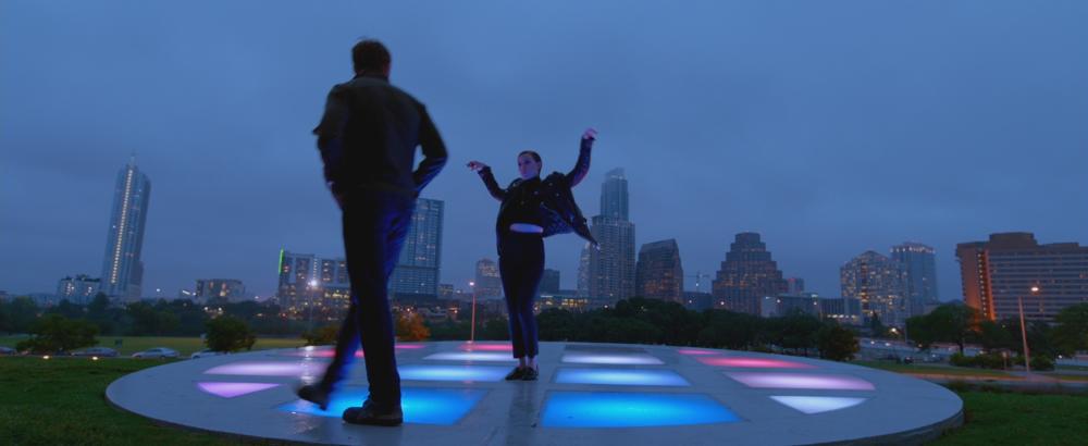 Song to Song screengrab, BV and Faye on the terrace at the Long Center. It is night, and the downtown Austin skyline is visible in the background