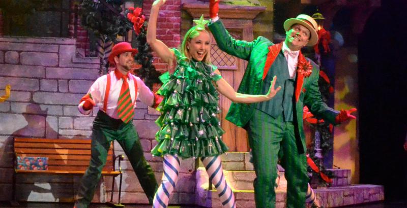 A female dressed as a Christmas tree performs on-stage with two males in holiday suits during the Alabama Theatre Christmas Special