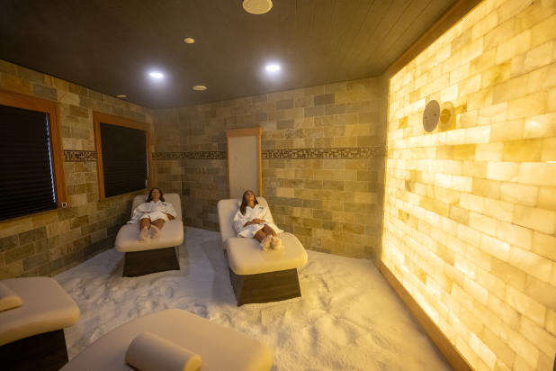 Two women wearing white robes laying on a spa table in a salt therapy room