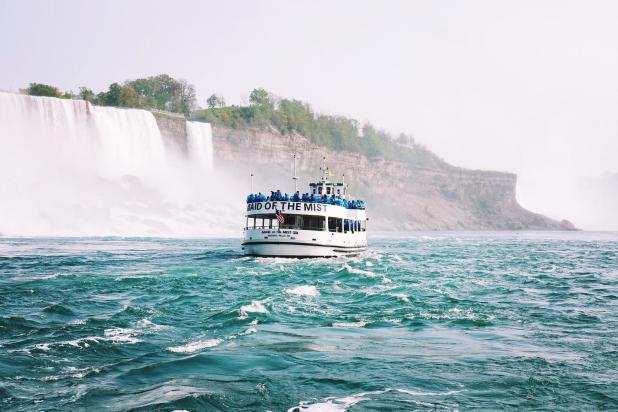 People in blue ponchos stand on the top deck of the Maid of the Mist boat tour as it passes by Niagara Falls