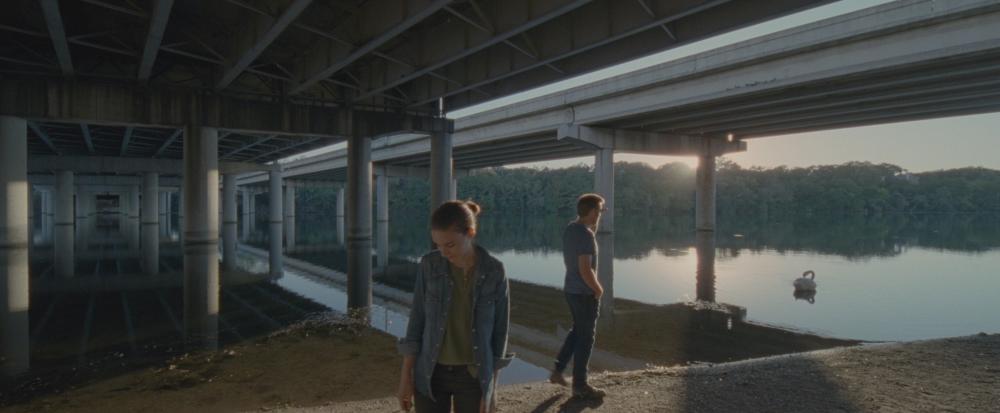 Song to Song screengrab, showing Faye and BV walking on a gravel trail under an IH35 overpass