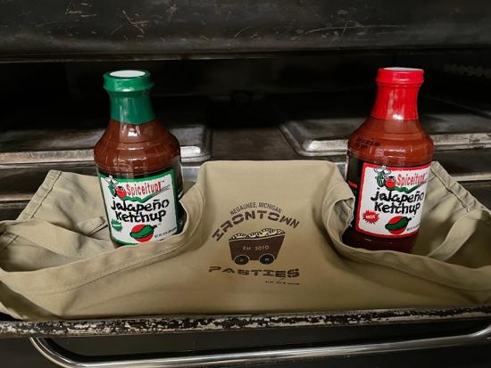 A staged photo of an Iron Town Pasty apron and two jalapeno ketchup bottles