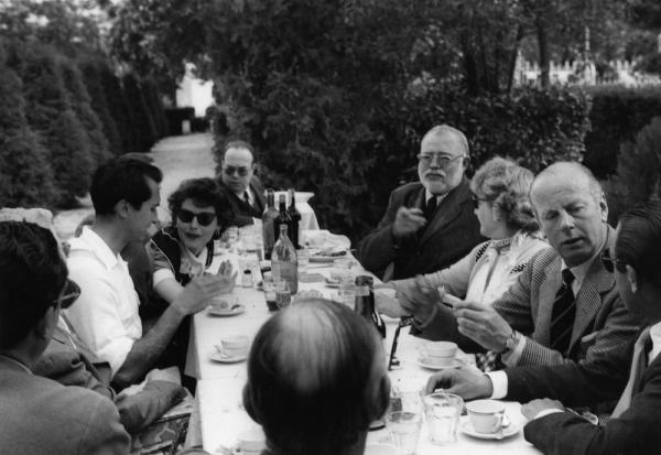 A dinner party in Spain with guests around a table outside. Guests include Ava Gardner, Luis Dominguin and Ernest Hemingway