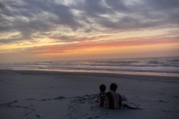 Two boys watching the sunrise on the beach