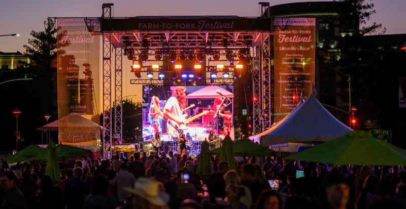 band performing on stage at night during the 2022 farm to fork festival with a crowd in the foreground