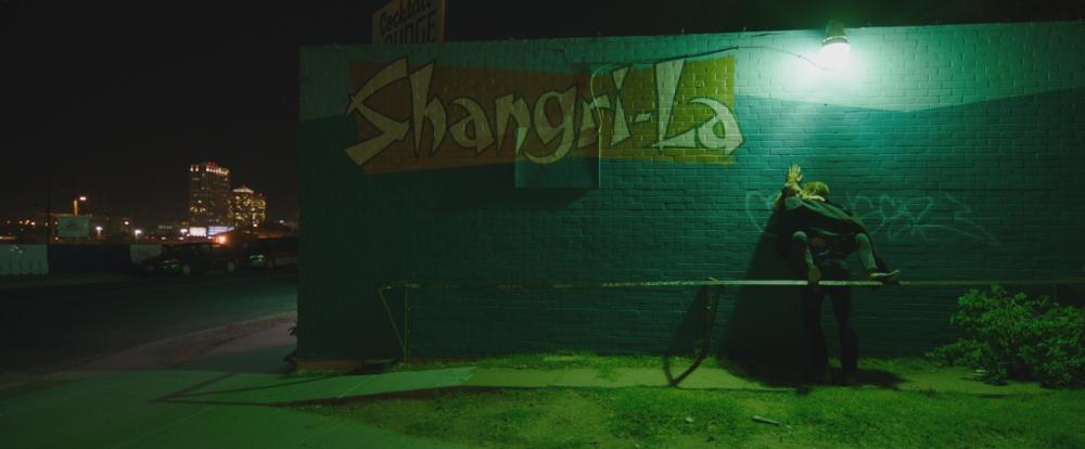 Song to Song screengrab, showing BV and Faye making out against the exterior wall of a bar with a mural that says Shangri-la