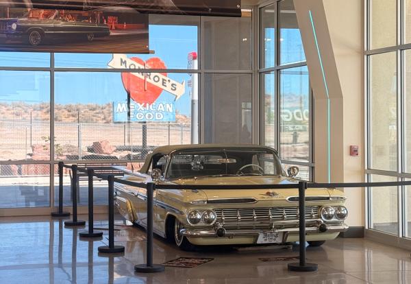 The foreground showcases a yellow lowrider car in the museum at the West Central Route 66 Visitor Center. In the background is a neon sign park.