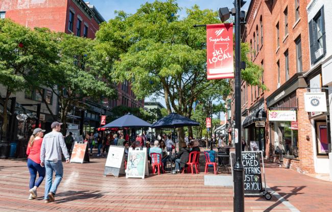 A sunny day on Church Street. People are out walking and enjoying outdoor restaurant seating under umbrellas.