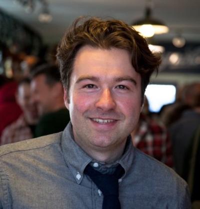 man smiles for camera wearing a shirt and tie.
