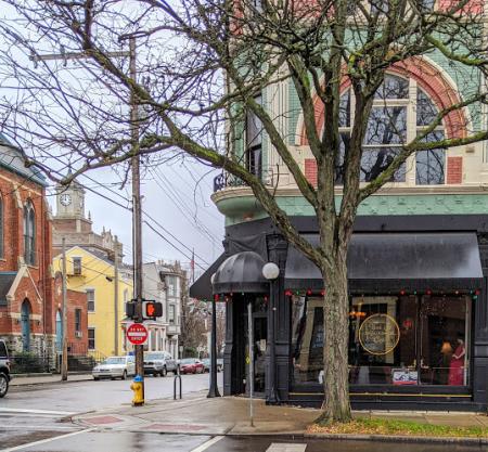 Exterior photo of York Street Cafe in Newport Ky with a view of the street, crosswalk, and a large tree in front of decorative archetecture and a black storefront awning