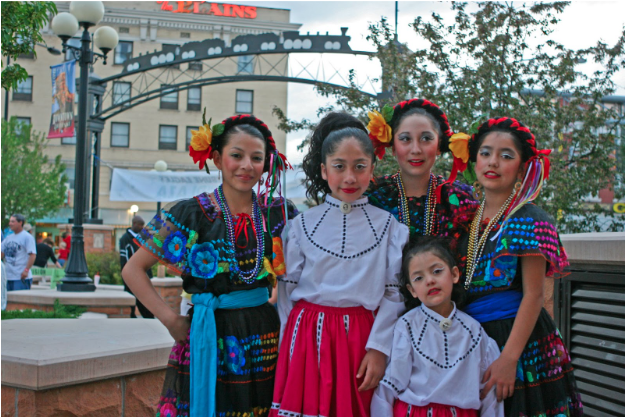 a group of young women dressed in celebratory dresses, hair and makeup for Cheyenne's Hispanic Festival
