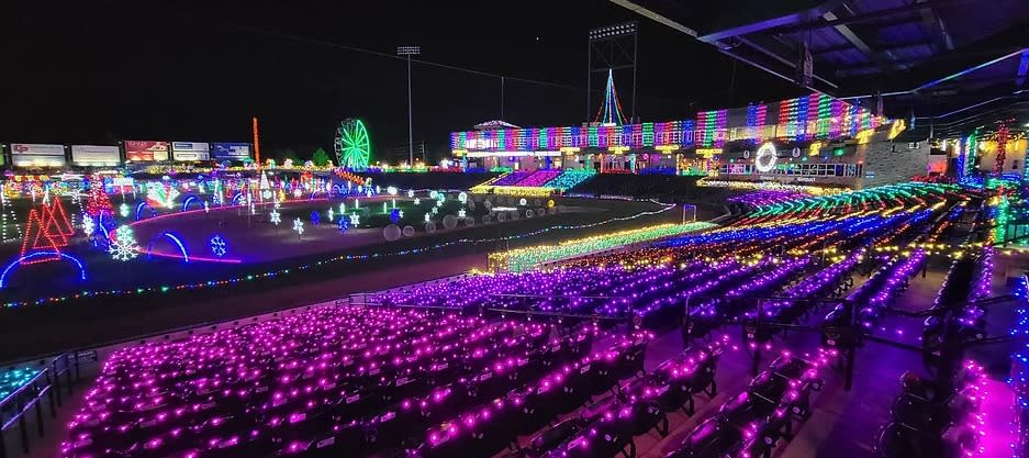 Nighttime display of holiday lights in pink, purple, green and yellow on the bleachers of the stadium.