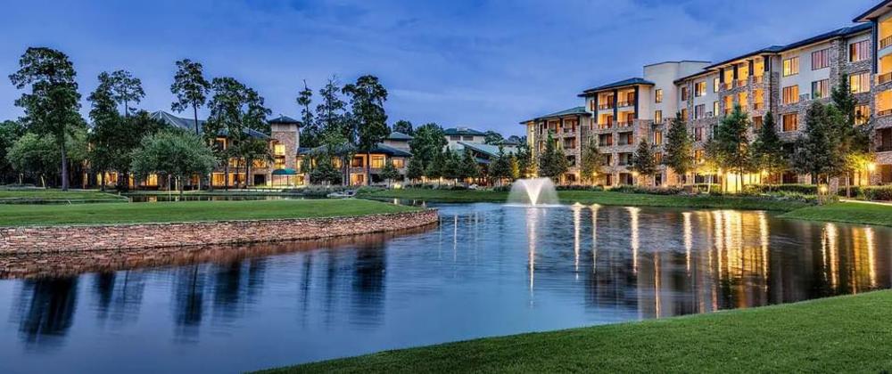 A wide-angle view of The Woodlands Resort in the evening. The photo is taken from the golf course, overlooking a sprawling pond toward The Resort welcome center, guest rooms, and restaurants.