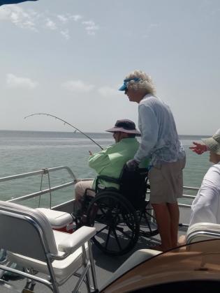Man fishing from his wheelchair being assisted