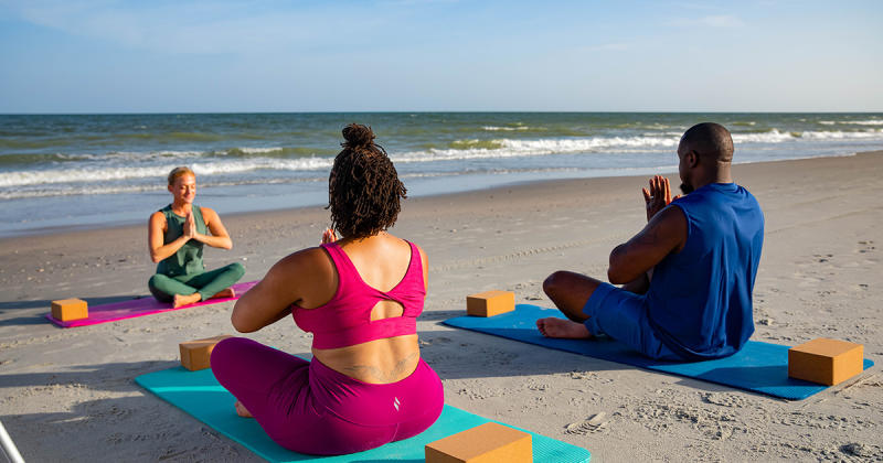 Three people doing yoga on the beach