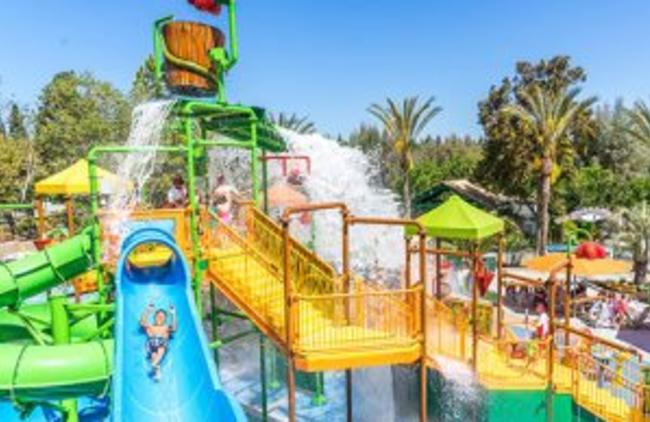 Family in line to go down a blue water slide while a boy is sliding down