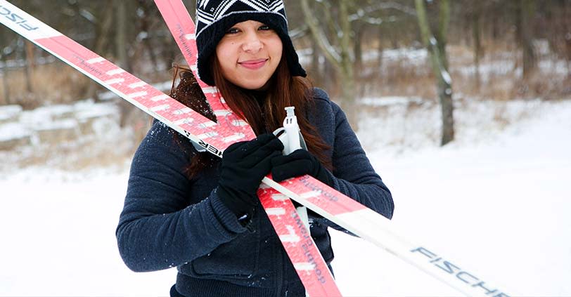 A young woman dressed in snow gear holds her skis over her shoulder in Busse Woods