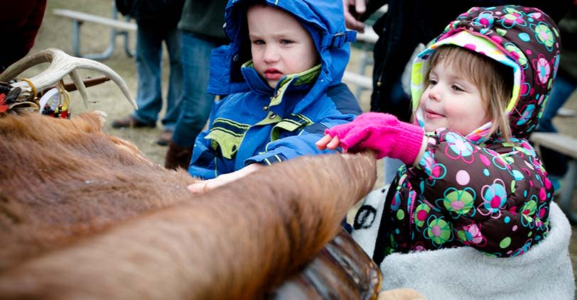 Two small children reach up to pet an elk in Busse Woods