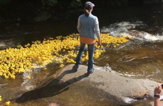 Woman Watching Hundreds of Yellow Rubber Ducks Float Down a River