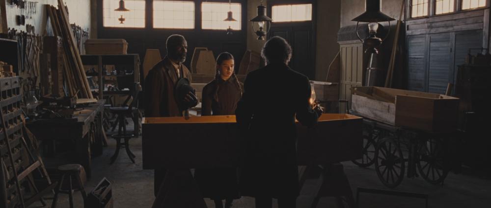 True Grit screengrab, showing two men and a young woman standing over a coffin inside the Fort Smith Undertakers Building