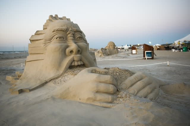 Sand sculpture showing a face gorging itself, mouth open, on a pile of sand.