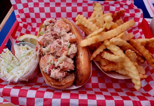 A lobster roll next to fries and a cup of cole slaw at Lobster Roll AKA Lunch