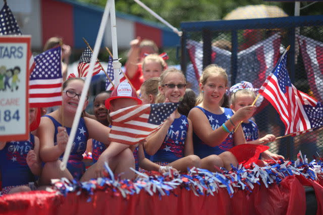 Several girls waving american flags during the Freedom Festival Parade in Greenwood, Indiana.