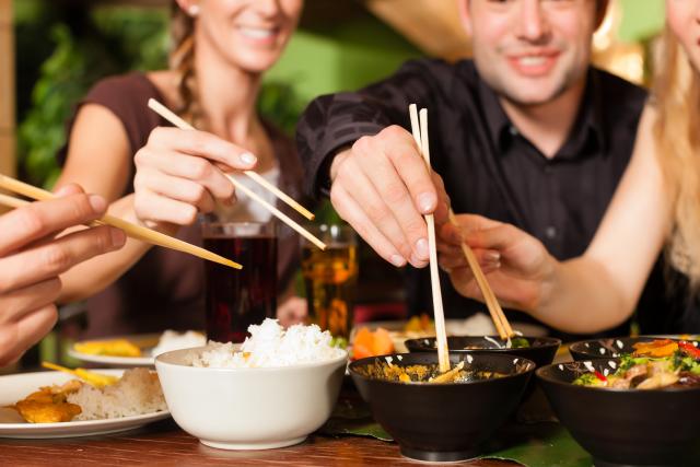 Friends share a meal while eating with chopsticks.