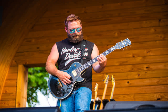 Man playing guitar on outdoor stage at festival.
