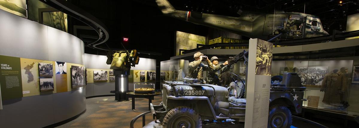 Huey helicopter hanging from ceiling and Army jeep with soldiers in a room surrounded by Vietnam war information and soldier profiles