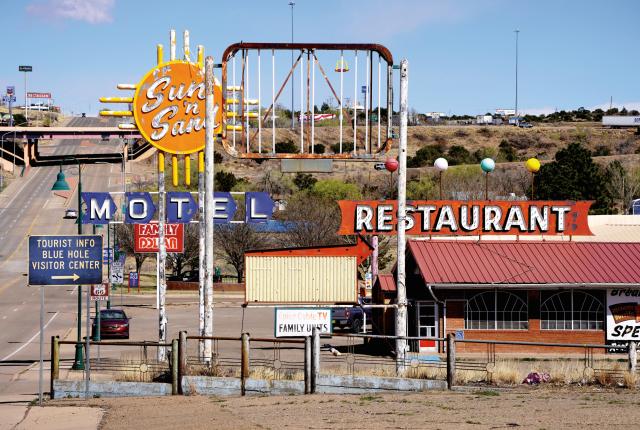 Vintage roadside scene with vibrant "MOTEL" and "RESTAURANT" signs, evoking nostalgia. Desert landscape and a highway add to the retro vibe.