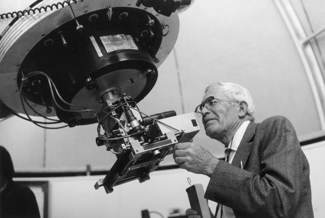 Person examining a large mechanical instrument inside a dome-like observatory.
