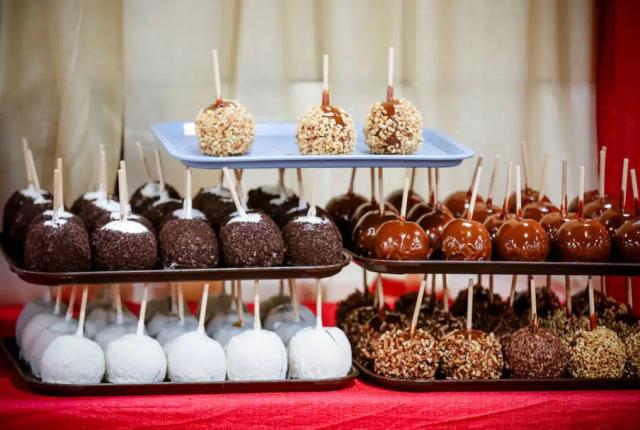 A variety of candy apples on tiered trays, featuring toppings like nuts, chocolate, and caramel.