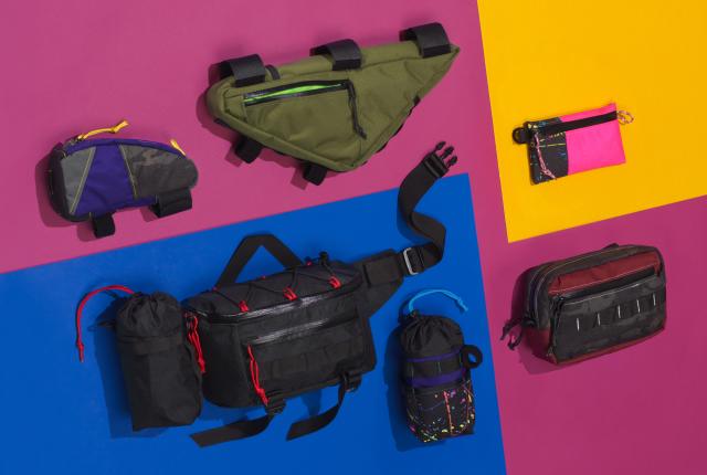 Seven colorful bags in different styles and sizes lay on a pink, blue, and orange background.