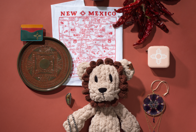 Flat-lay of New Mexico-made products from ABQ Collective, including chile ristras, jewelry, a plush lion toy, honey, and local art items.