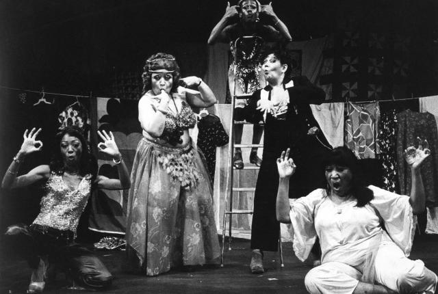 Black and white photo of five costumed performers posing energetically on stage.