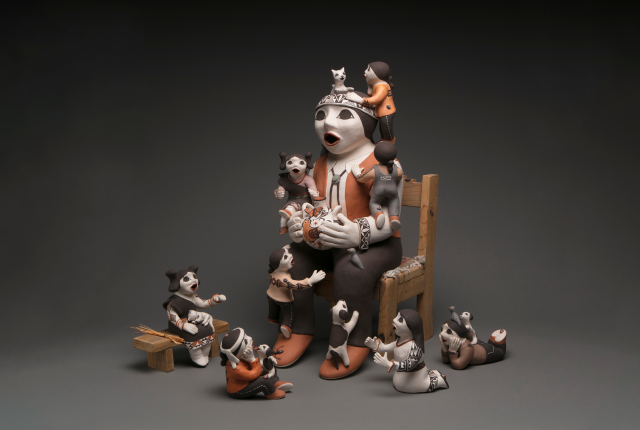 Clay storyteller figure seated on a chair, surrounded by many small child and animal figures climbing, sitting, and interacting around the central figure.