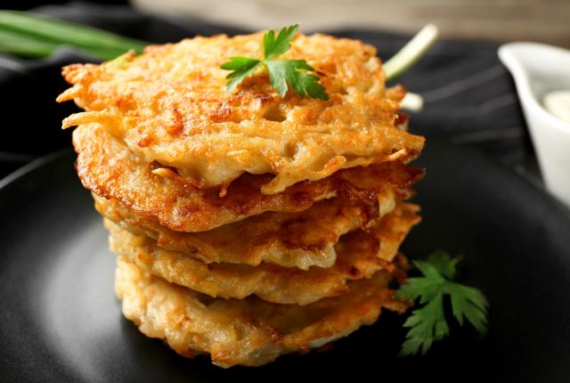 A stack of golden brown potato pancakes topped with parsley sits on a black plate.