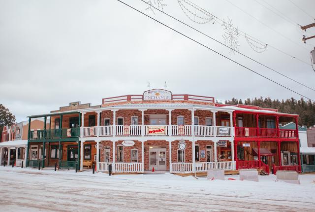 A snow-covered street lined with old-fashioned shops with balconies on a cloudy day.