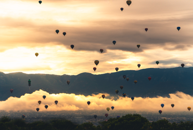 Hot-air balloons floating up at sunrise with the Sandia Mountains in the background.