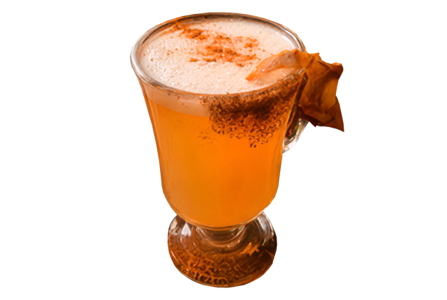 Amber drink topped with white foam and a dusting of cinnamon in a clear footed mug.