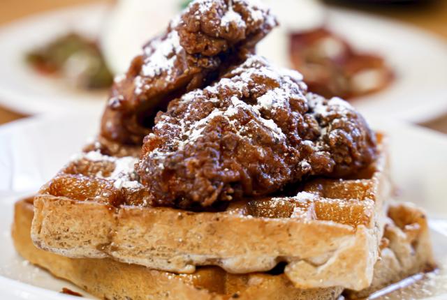 A plate with a waffle topped with crispy fried chicken and powdered sugar.