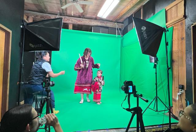Two people pose in front of a green screen during a photoshoot.