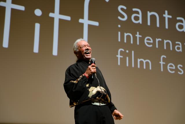 Person speaking onstage with a microphone in front of a Santa Fe International Film Festival screen.