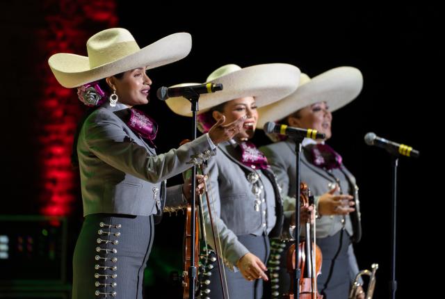 Woman mariachi members singing on stange and holding their violin instruments.