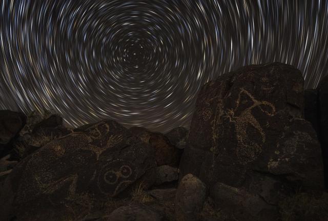 Petroglyphs on dark rocks under a swirling night sky create a mystical atmosphere.